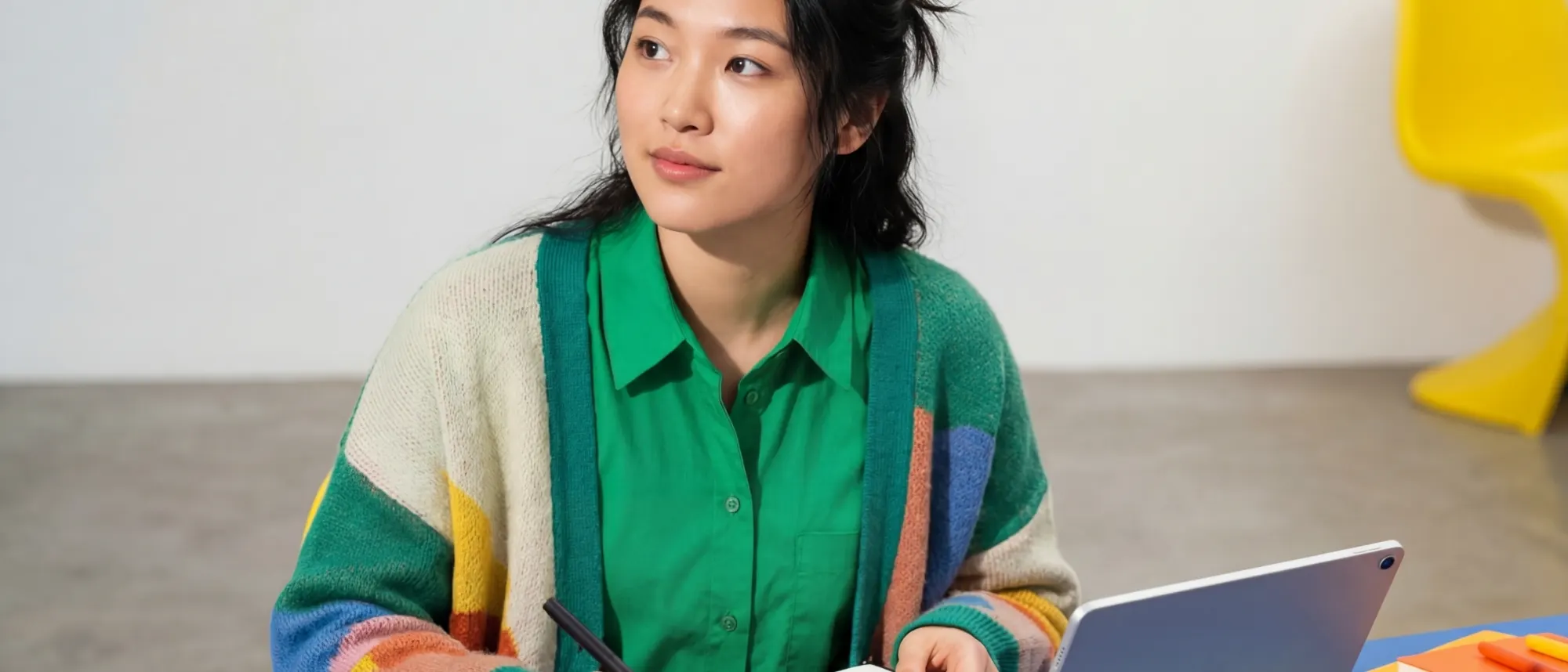 A woman pausing mid-thought at a desk with a notebook and tablet