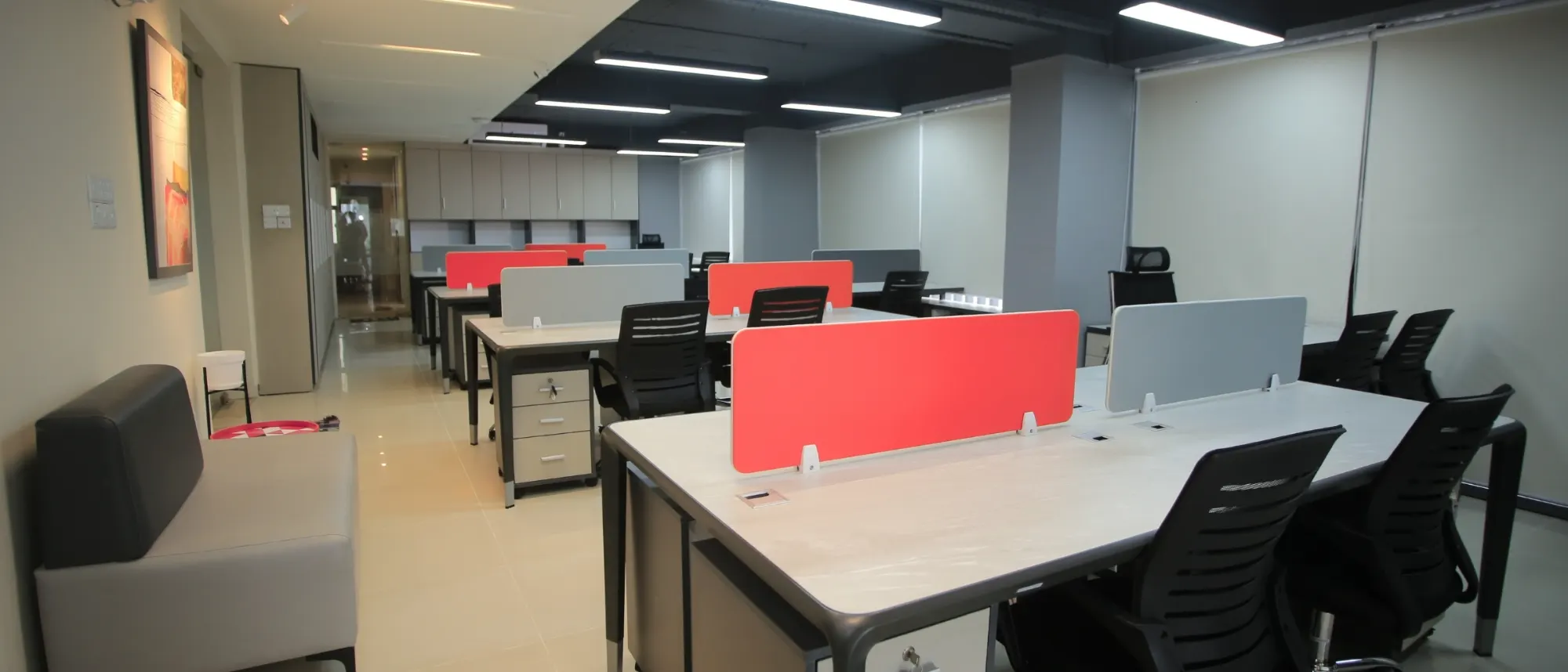 An empty open-plan office with rows of desks and red dividers